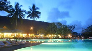 A nighttime view of a resort pool with lounge chairs and palm trees. - Mnarani Beach Club (Malindi)