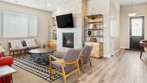 A living room with a fireplace, a flat-screen TV, a ceiling fan, and a dining area. - Snow Canyon Paradise #46 by RedAwning (Ivins)