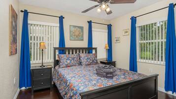 A bedroom with a bed, two bedside tables, a ceiling fan, and curtains.