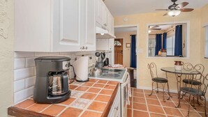 A compact kitchen with white cabinets, a coffee maker, and a stove. There is a dining area with metal chairs and a small table.