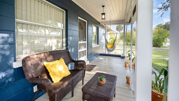 A covered porch with a wicker sofa, a small table, and a hanging chair.