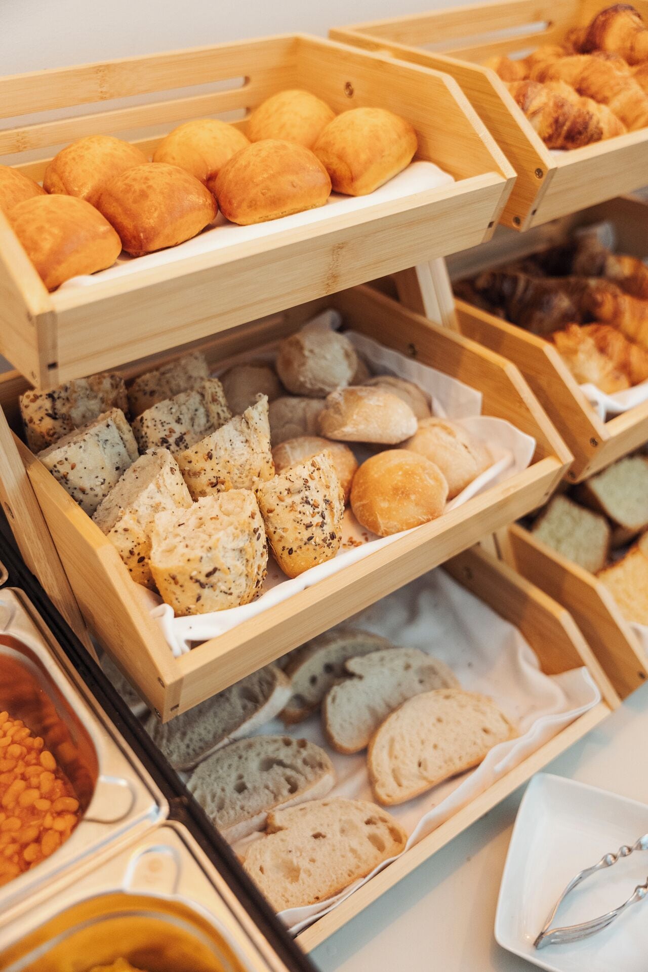 A variety of baked goods in wooden trays, including bread rolls and sliced bread with herbs.