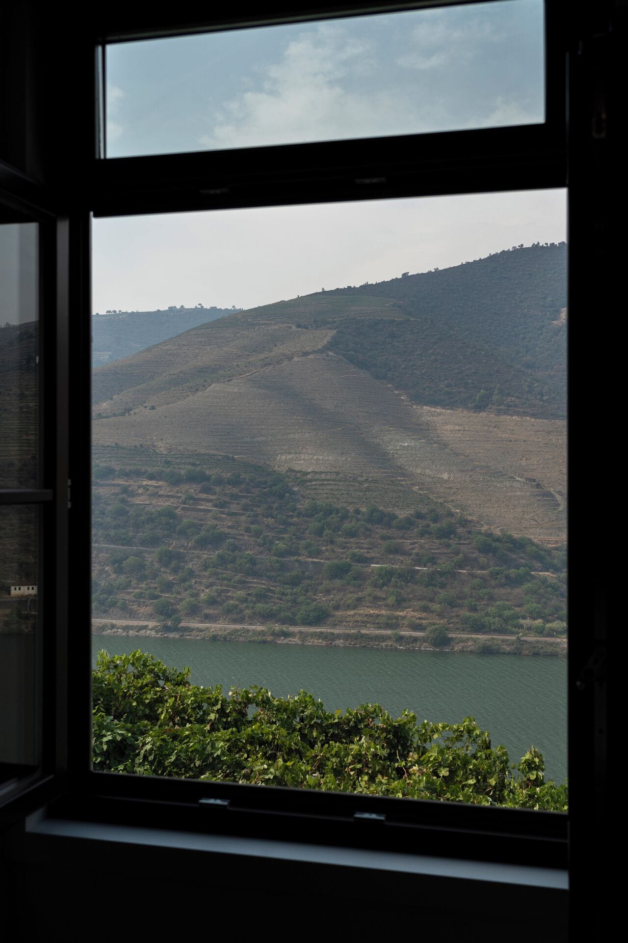 A view through a window of a hilly landscape with a body of water in the foreground.