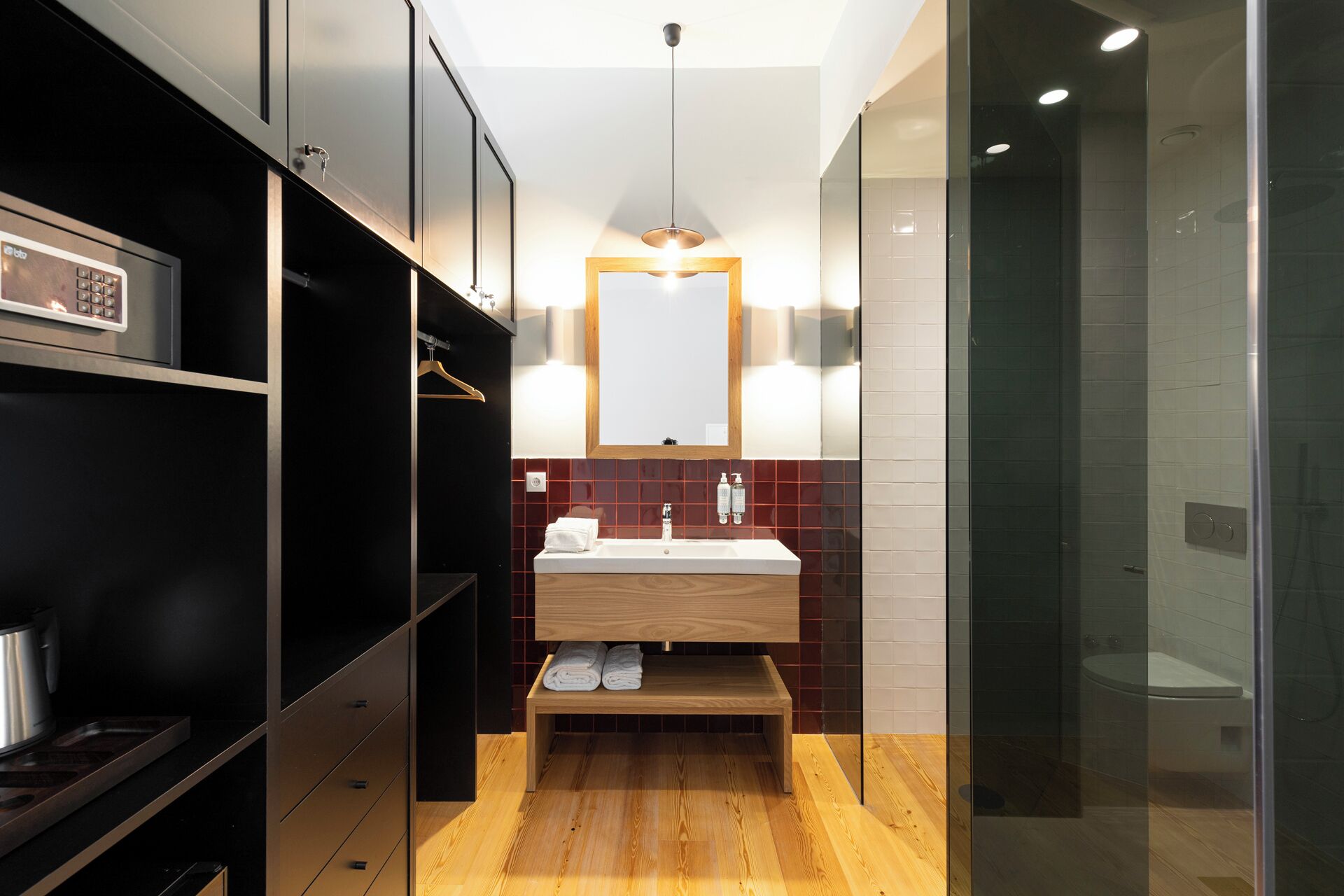 A modern bathroom with a wooden vanity, a glass shower enclosure, and a black shelving unit.