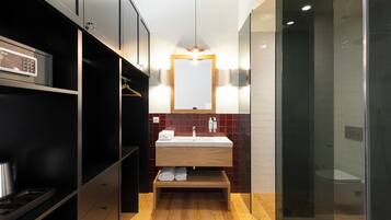 A modern bathroom with a wooden vanity, a glass shower enclosure, and a black shelving unit.