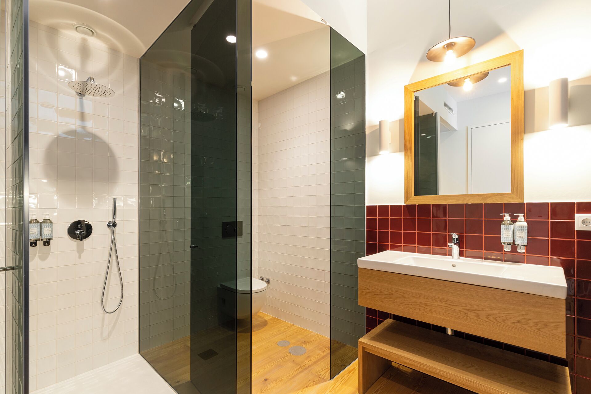 Un baño moderno con ducha envuelta en vidrio, tocador de madera y espejo con luces integradas en la pared.
