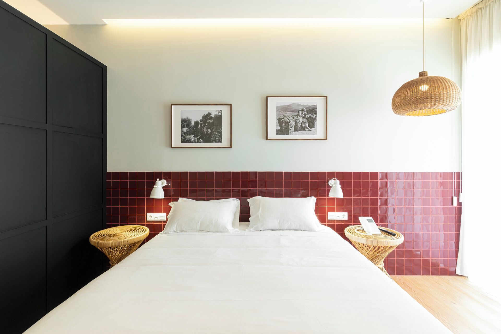 Ein Hotelzimmer mit einem großen Bett, zwei an der Wand befestigten Bilderrahmen, einem roten Kachelbettkopfs und zwei Nachttischen mit Lampen.