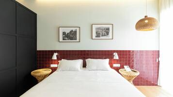 Ein Hotelzimmer mit einem großen Bett, zwei an der Wand befestigten Bilderrahmen, einem roten Kachelbettkopfs und zwei Nachttischen mit Lampen.