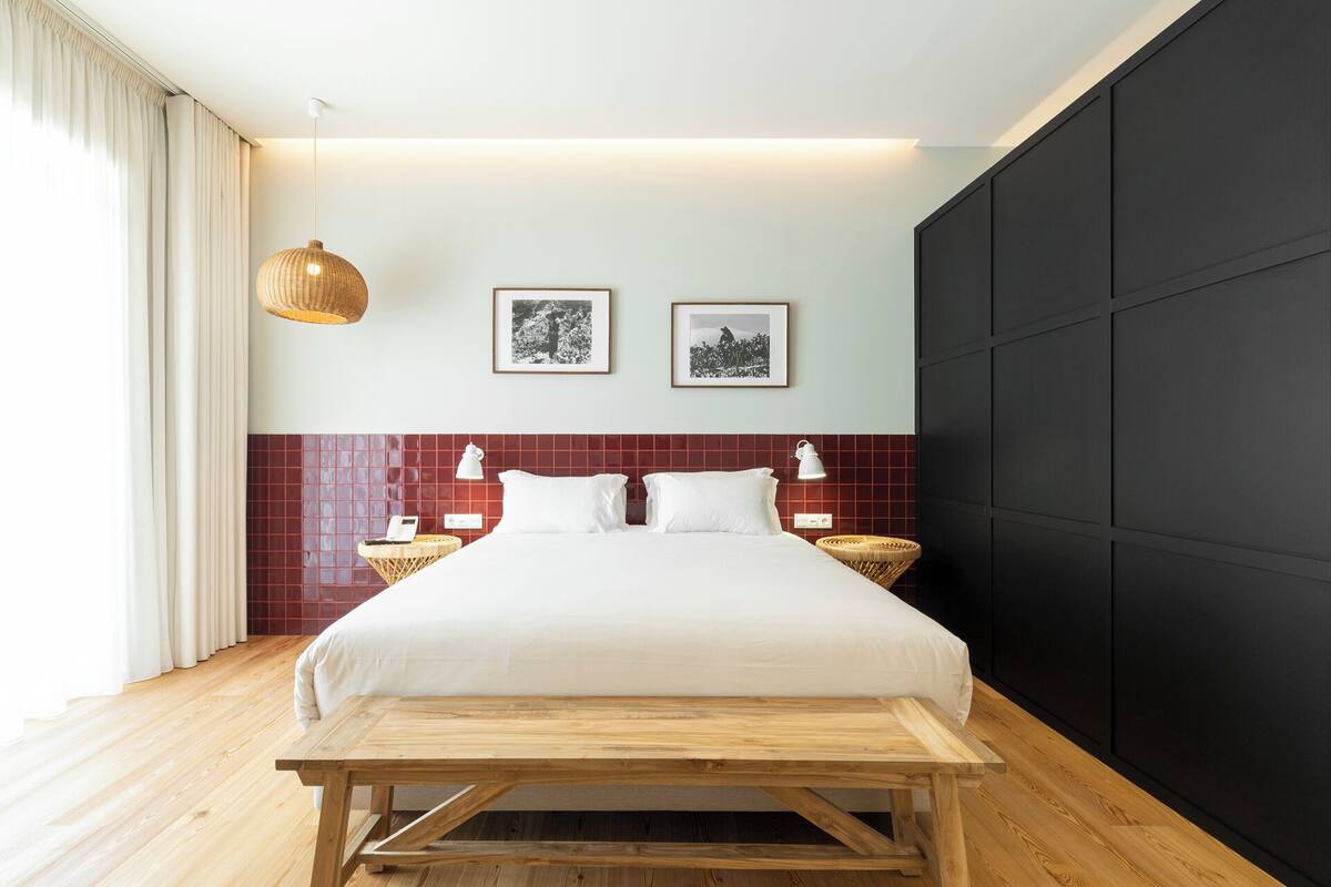 Ein modernes Schlafzimmer mit einem großen Bett, zwei Nachttischen, einer hölzernen Bank, einem roten Kachel-Kopfende und zwei gerahmten Bildern an der Wand.