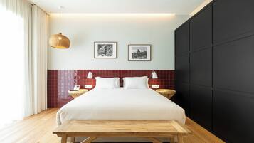 Un dormitorio moderno con una cama grande, dos mesitas de noche, un banco de madera, un cabecero de azulejos rojos y dos cuadros enmarcados en la pared.