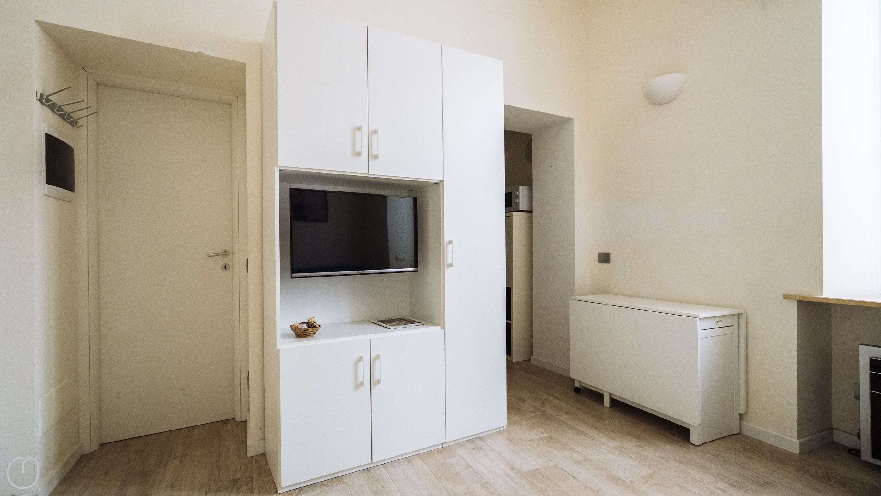 A compact living space with a white wardrobe, a flat-screen TV, and a small radiator.