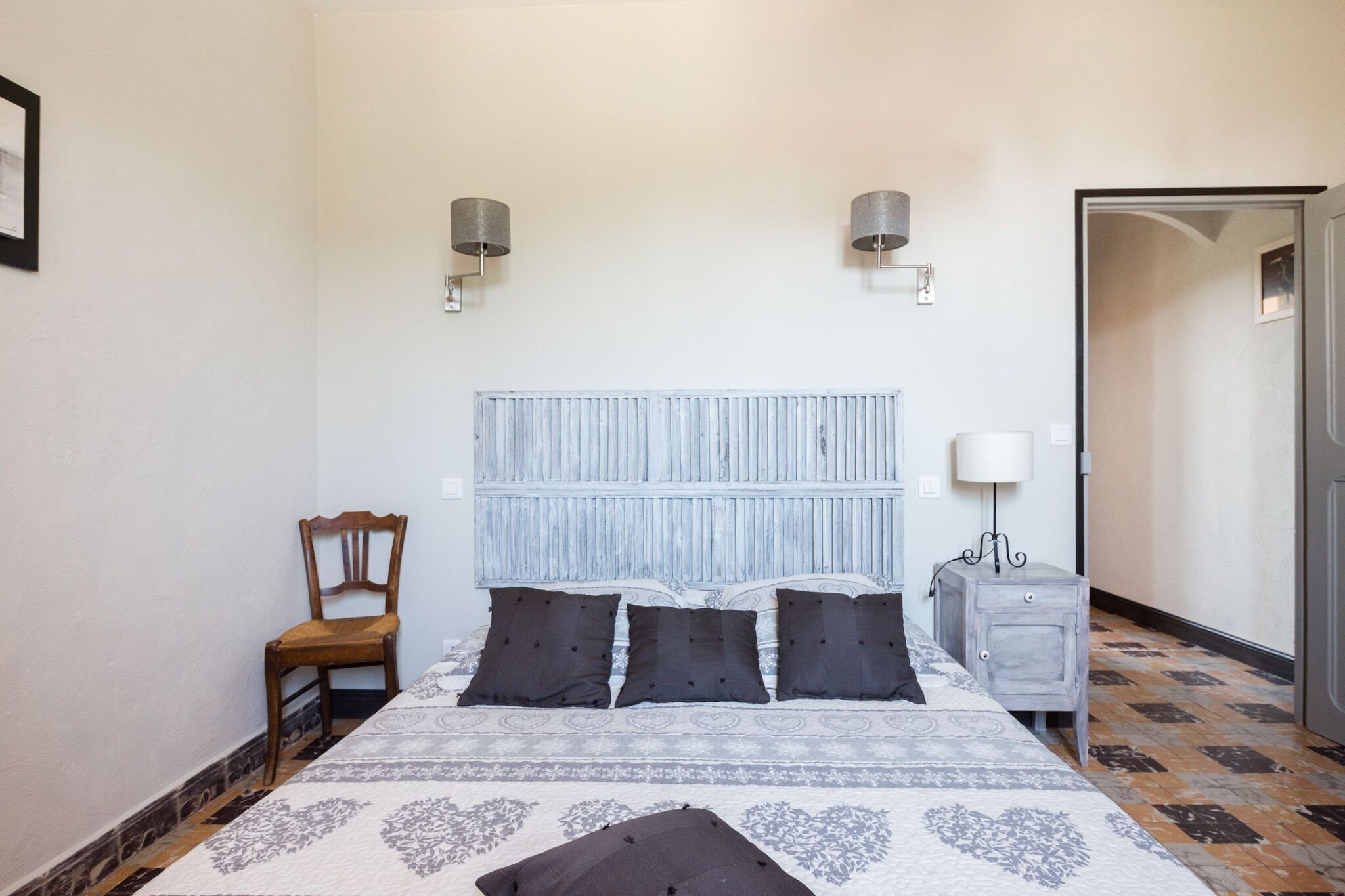A bedroom with a bed, a chair, a nightstand, and a door.