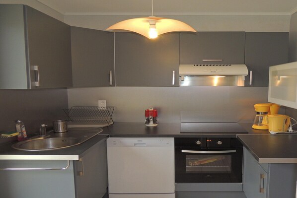 A compact kitchen with grey cabinets, a dishwasher, an oven, a microwave, and a coffee maker.