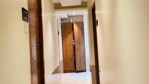 A hallway with a wooden door at the end, a light switch on the wall, and a tiled floor. - Hotel Regal Inn (Mumbai)