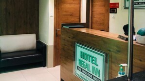 A hotel reception area with a wooden reception desk, a check-out counter, and a reception desk with a sign indicating the hotel is owned by Royal Inn. - Hotel Regal Inn (Mumbai)