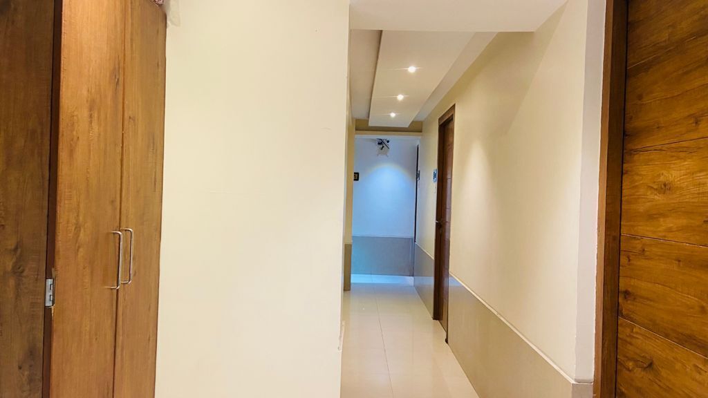 Un pasillo con puertas de madera y suelo de baldosas, que conduce a una habitación con ventilador de techo e iluminación empotrada.