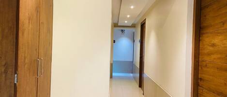 Un pasillo con puertas de madera y suelo de baldosas, que conduce a una habitación con ventilador de techo e iluminación empotrada.