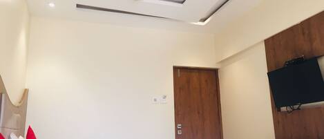 Ein Hotelzimmer mit einem Bett, einem Deckenventilator, einer Holztür und einem an der Wand befestigten Fernseher.