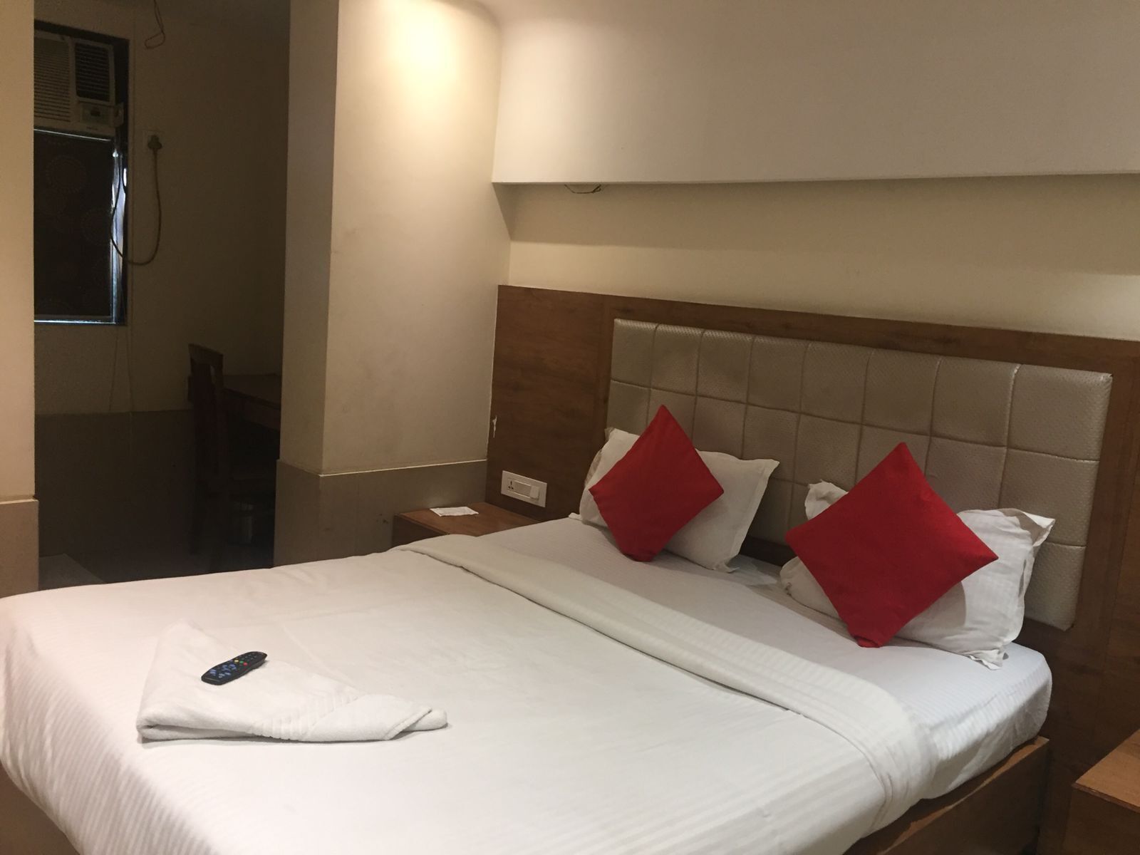 A hotel room with a large bed, two red pillows, a remote control, and a wooden headboard.