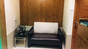 A small room with a dark leather sofa, a standing fan, and a wooden wall. - Hotel Regal Inn (Mumbai)