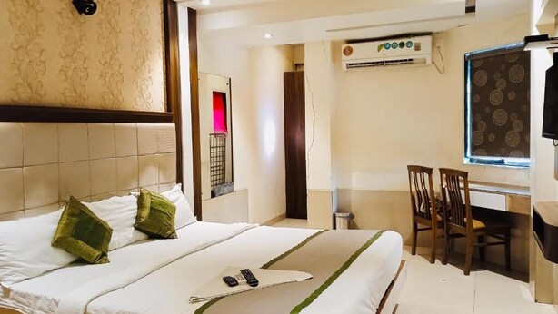 A hotel room with a bed, a desk, and a chair. There is an air conditioning unit on the wall and a window with a view. - Hotel Regal Inn (Mumbai)