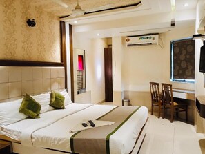 Habitación de hotel con cama, escritorio y silla. Se observa una unidad de aire acondicionado en la pared y una ventana con vistas.