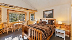 Une chambre à coucher en bois, avec un lit, un bureau et une chaise, de grandes fenêtres et un tableau accroché au mur.