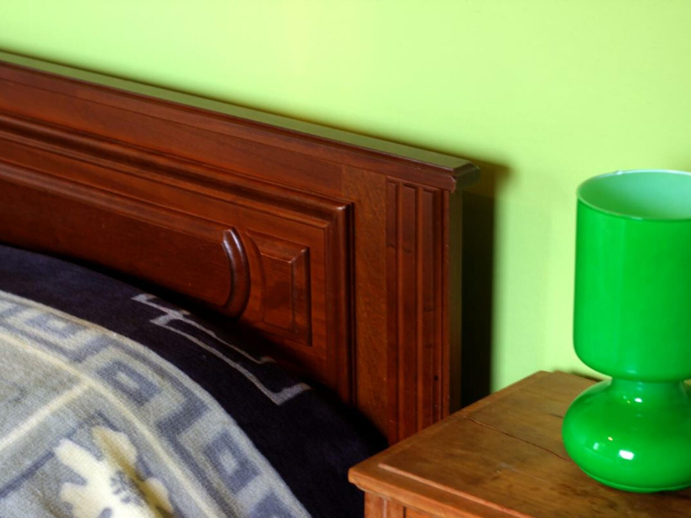 A wooden headboard with a dark blanket and a green object on a wooden nightstand.