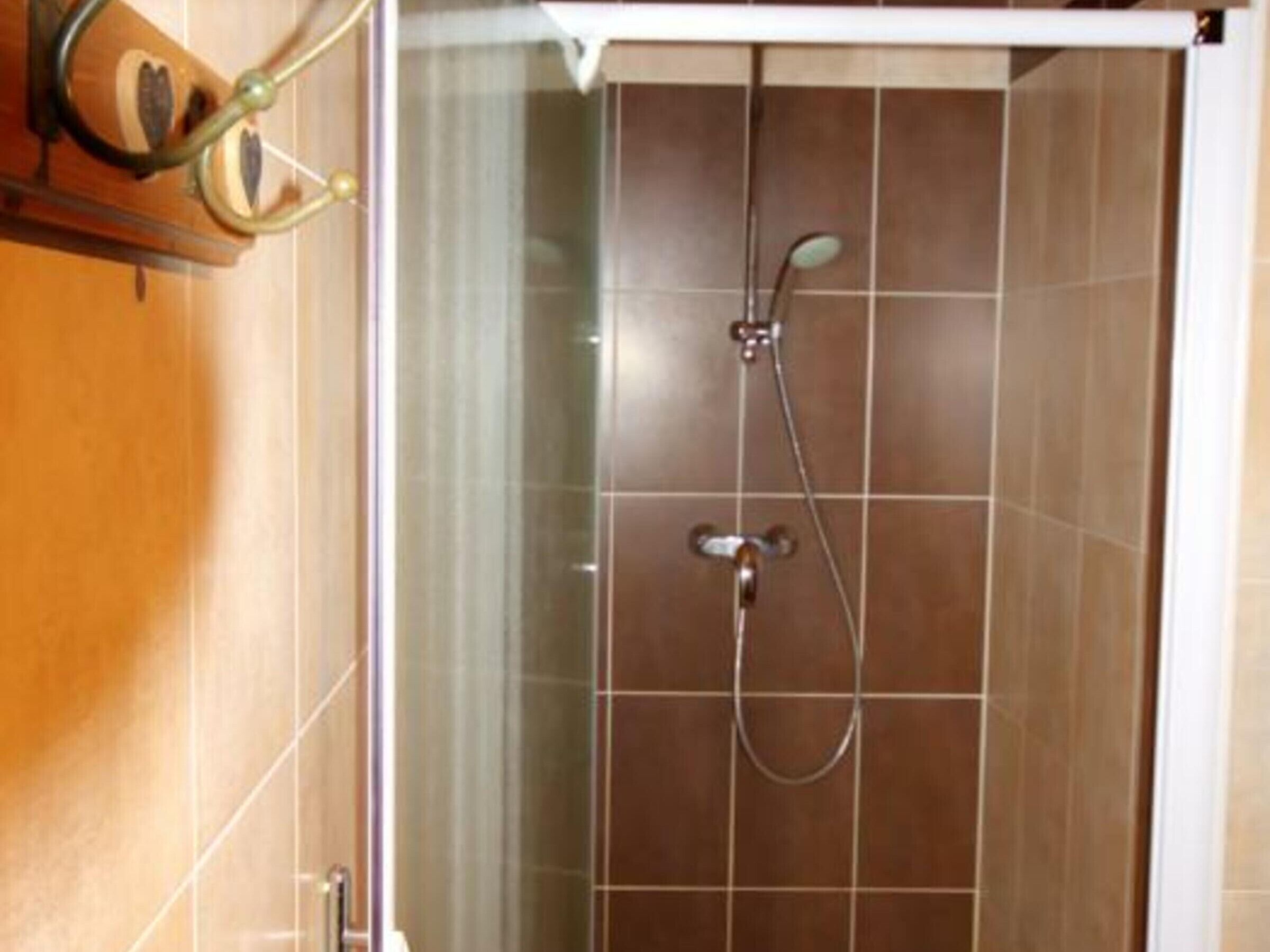 Una doccia con porta in vetro, soffione a mano e rubinetto a muro.