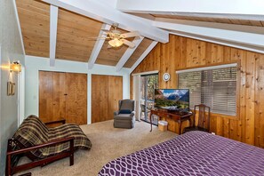 A bedroom with a wooden ceiling, a bed with a patterned bedspread, a desk with a computer, a chair, and a television. - Whispering Cottage by Destination Big Bear: Walk to Meadow Park & Lake from this Summit Lake Home! Pet Friendly! Fully Fenced Yard! (Big Bear Lake)