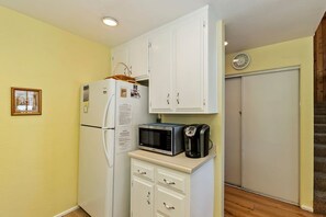 Una cocina compacta con refrigerador, microondas y cafetera sobre una pequeña encimera.