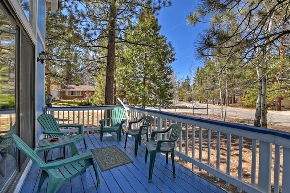 A wooden deck with green chairs and a table, overlooking a forested area.