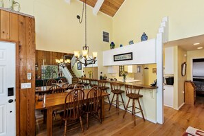 Una cocina amplia con piso de madera, un comedor con sillas de madera, una araña y una escalera que conduce a otro nivel.