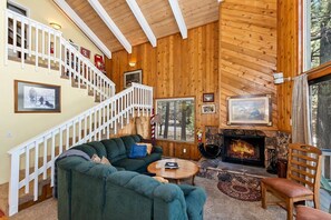 A cozy living room with a fireplace, a staircase, and a large window.