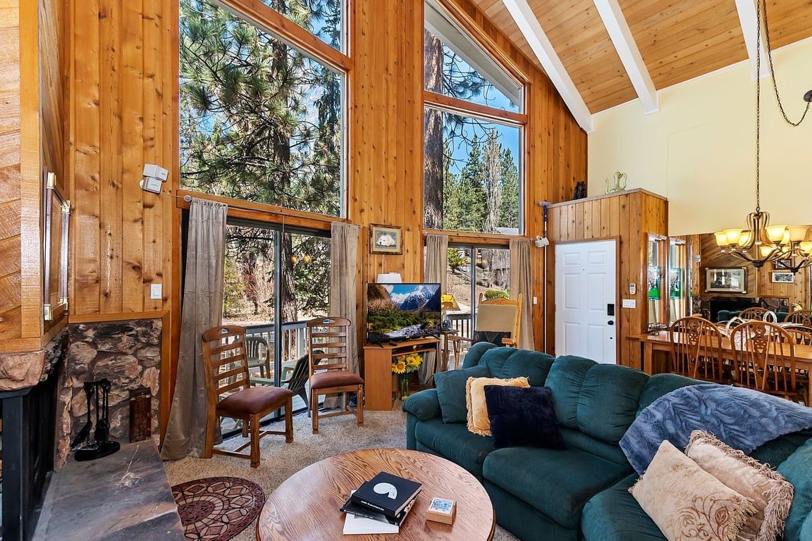 A cozy cabin interior with a stone fireplace, a green sofa, and a dining area with wooden furniture.