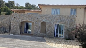 A stone facade with arched doorways and large windows, a wooden deck, and a tiled patio area. - Villa between sea and mountains 15 minutes from the beach (zonza)