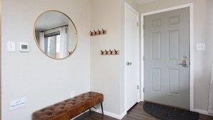 A hallway with a bench, a round mirror, a coat rack, a door, and a thermostat. - Modern Chic Retreat | Near Mtns & Red Rocks | Wifi (Wheat Ridge)