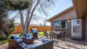 A backyard with outdoor furniture, a grill, and a house with a large window. - Modern Chic Retreat | Near Mtns & Red Rocks | Wifi (Wheat Ridge)