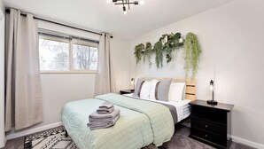 A bedroom with a bed, bedside tables, a window with curtains, a wall-mounted plant, and a patterned rug. - Modern Chic Retreat | Near Mtns & Red Rocks | Wifi (Wheat Ridge)