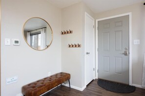 A hallway with a bench, a round mirror, a coat rack, a door, and a thermostat. - Modern Chic Retreat | Near Mtns & Red Rocks | Wifi (Wheat Ridge)