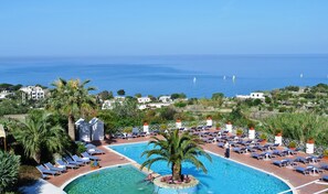 Piscina de resort con tumbonas, una palmera y vista al mar.