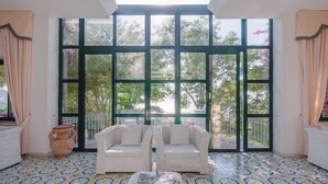 Una habitación con un ventanal grande, sofá de mimbre, baldosas de suelo estampadas y un jarrón.