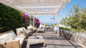 Un patio al aire libre con mobiliario de mimbre, un pérgola y vista al mar.