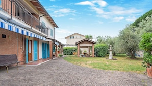 Une cour avec un chemin pavé, un banc, une petite fontaine et un bâtiment doté d’un balcon.