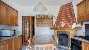 Une cuisine avec des meubles de rangement en bois, une table à manger, un four à micro-ondes, une cheminée et un luminaire suspendu.