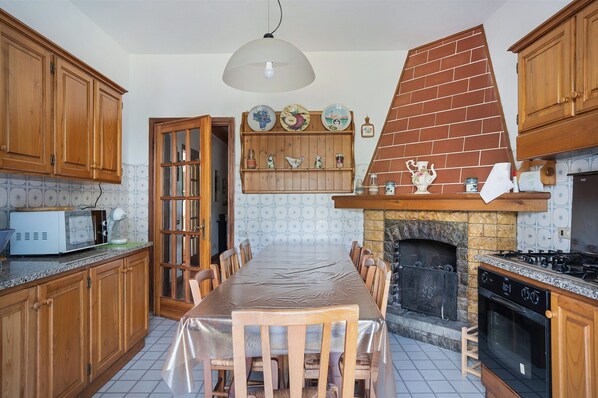 Cozinha com armários de madeira, mesa de jantar, micro-ondas, lareira e luminária pendente.
