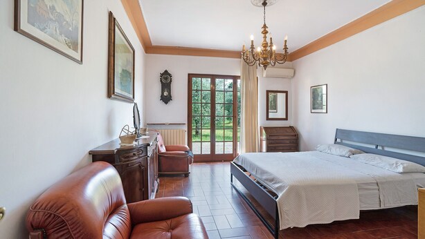 Une chambre à coucher comprenant un lit, un fauteuil en cuir, une commode et un lustre.