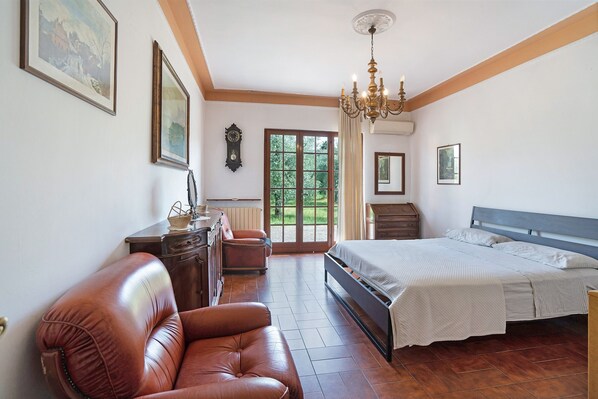 Un dormitorio con cama, una butaca de cuero, cómoda y candelabro.