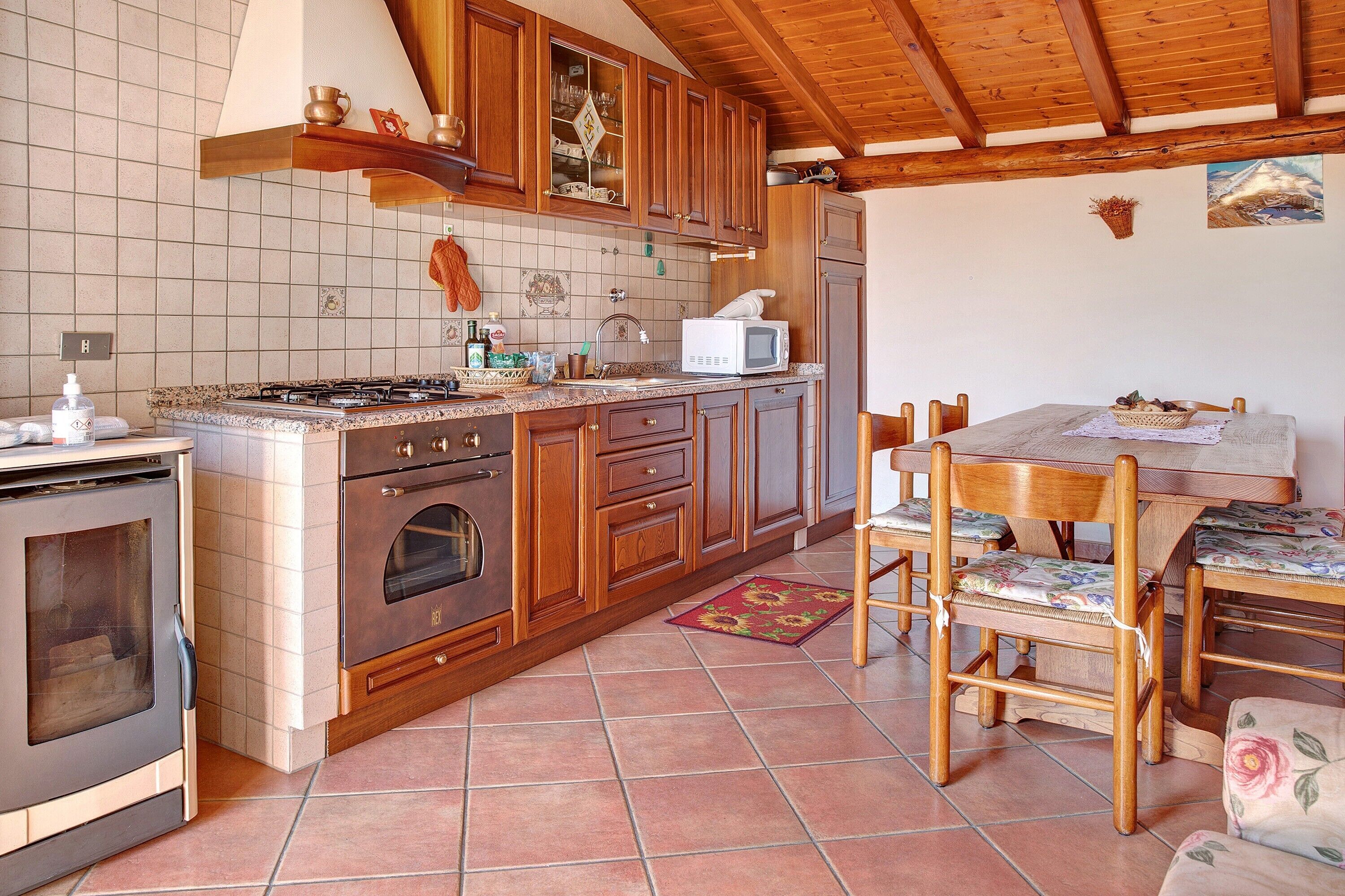 Een keuken met houten kastjes, een fornuis, een magnetron en een eethoek met een tafel en stoelen.
