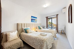 Habitación de hotel con dos camas, un sofá, una silla, un cuadro y vistas al exterior.